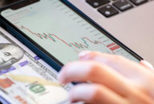 Close-up of a smartphone displaying stock market data over a dollar bill on a desk.